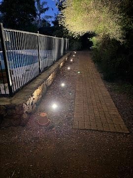 Low-voltage garden pathway lighting installed along a poolside path at dusk